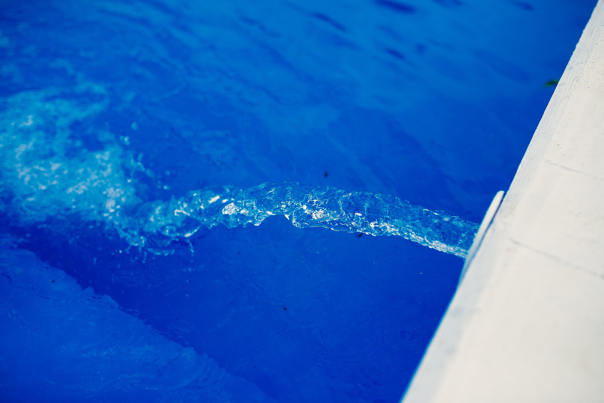 Calm blue water with soft ripples beside the white edge of a swimming pool